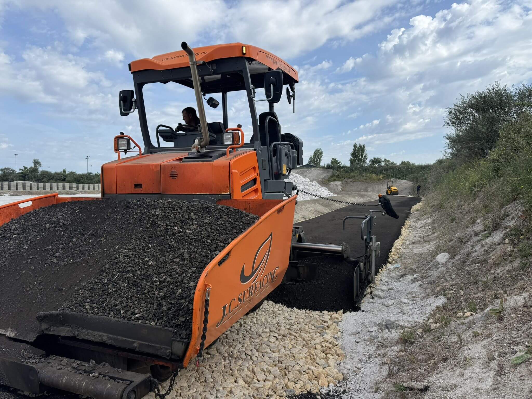 JC Surfacing paving machine spreading asphalt on construction site JC Surfacing paving machine spreading asphalt on construction site